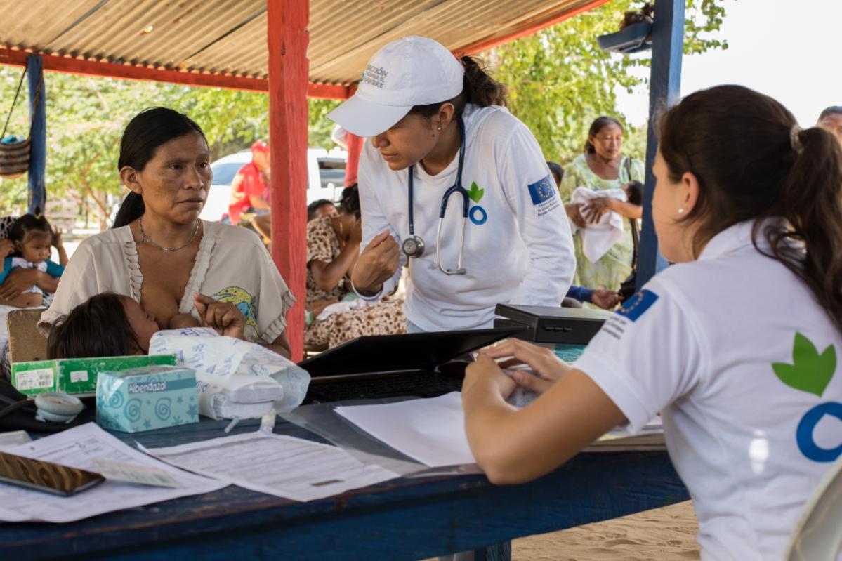 Mujer en Colombia amamanta a su hijo mientras dos personas le explican algo